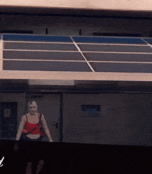 a woman in a red tank top is walking in front of a building with a sign that says emergency on it