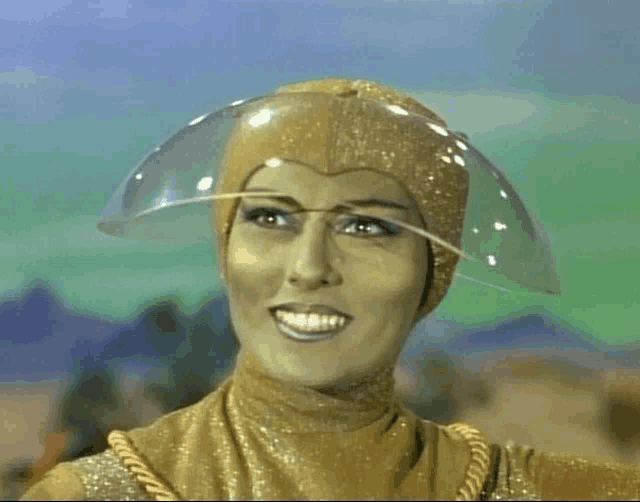 a woman in a gold costume is smiling and wearing a clear helmet on her head .