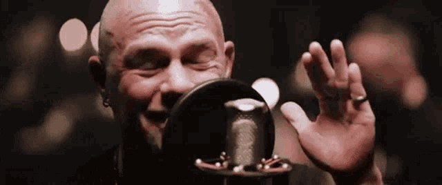 a bald man singing into a microphone with his eyes closed .