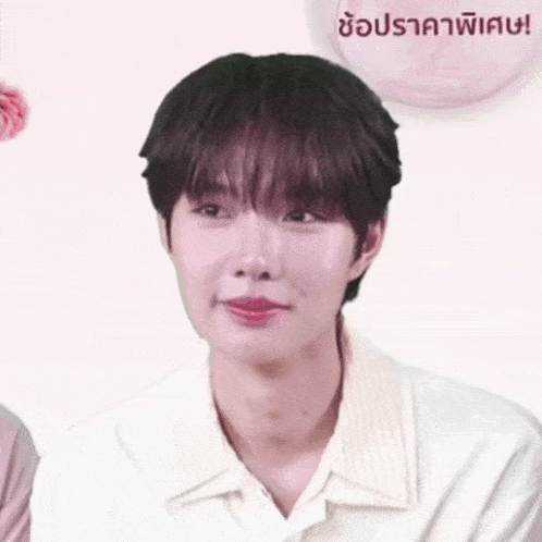 a man in a white shirt making a funny face with a pink balloon in the background with a foreign language written on it