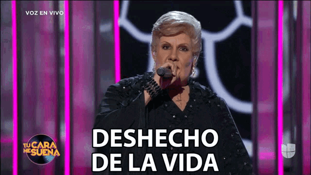 a woman singing into a microphone with the words deshecho de la vida on the screen behind her