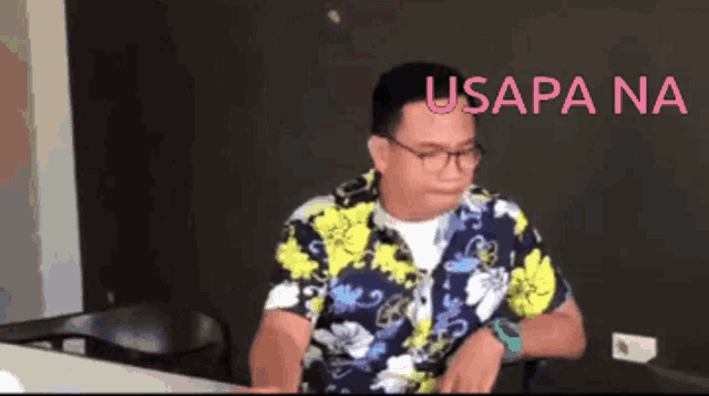a man wearing glasses and a hawaiian shirt is sitting at a desk with usapa na written on the bottom