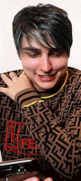 a man with green hair is wearing a fendi sweater and looking at his phone .