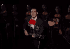 a man in a mariachi outfit is holding a guitar in front of a band