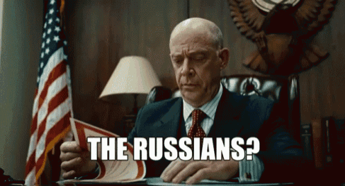 a man in a suit and tie is sitting at a desk reading a book with the words the russians written below him