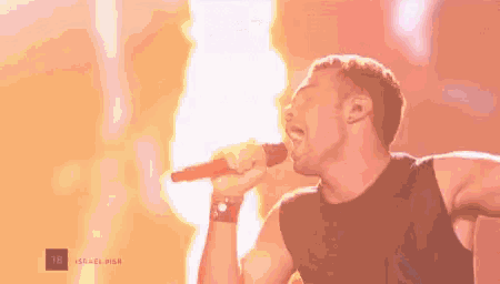 a man is singing into a microphone while a fire is behind him .