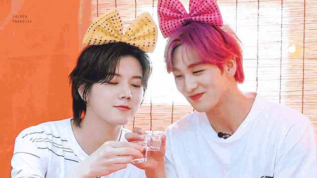 two young men wearing bows on their heads are drinking from a glass