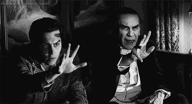 two men are sitting on a couch with their hands up in a black and white photo