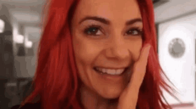 a woman with red hair is smiling while touching her face .