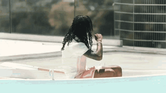 a man with dreadlocks is sitting in a small boat in a pool .