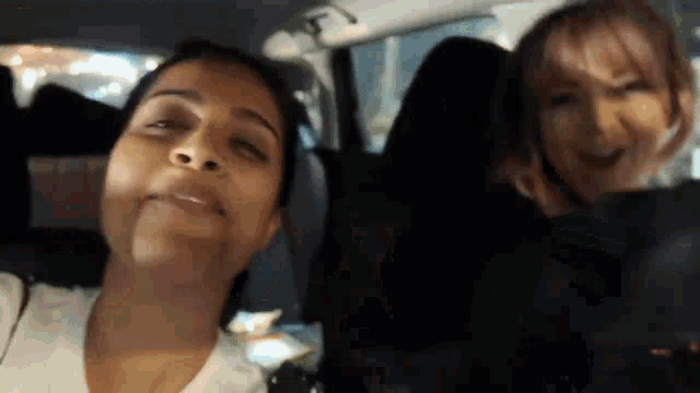 two women are sitting in the back seat of a car and smiling at the camera