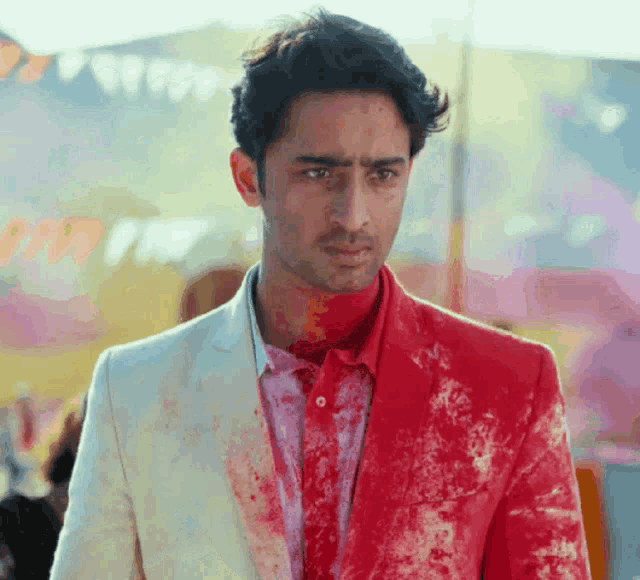 a man wearing a white suit and a red shirt is covered in red paint