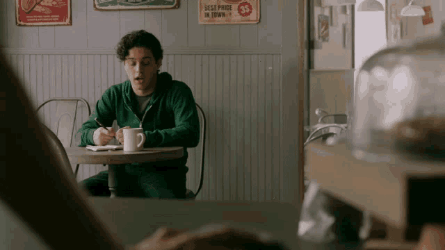 a man sits at a table in front of a sign that says ' best price in town ' on it