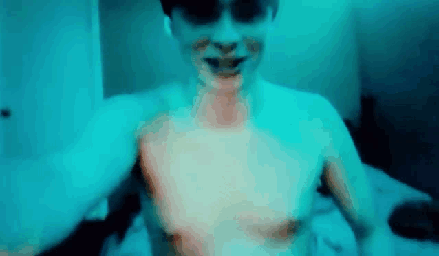 a man without a shirt is laying on a bed with a blue light behind him