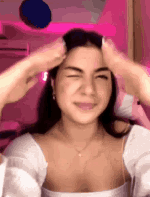 a woman is making a funny face while holding her head in front of a pink background .