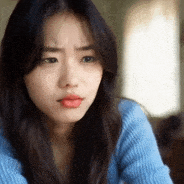 a woman wearing a blue sweater is making a sad face