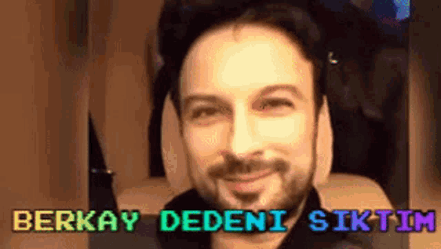 a man with a beard is smiling and looking at the camera while sitting in a chair .