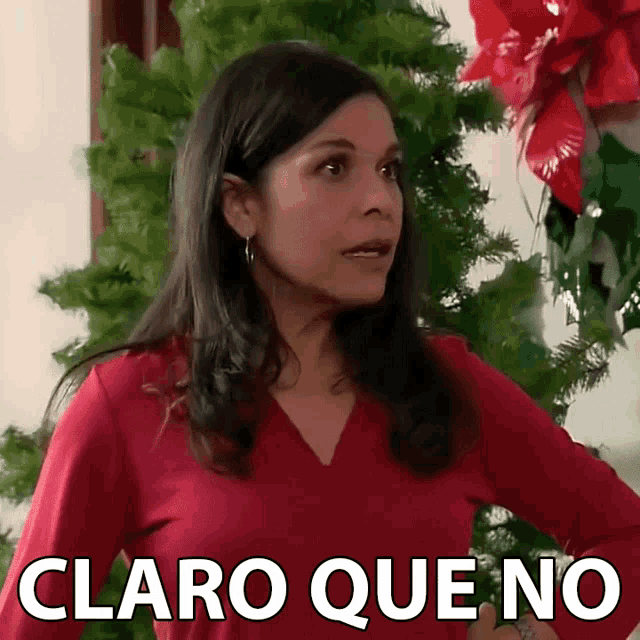 a woman in a red shirt stands in front of a christmas tree and says claro que no in white letters