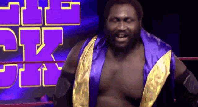 a wrestler in a blue and yellow robe is standing in a wrestling ring with a purple background behind him .