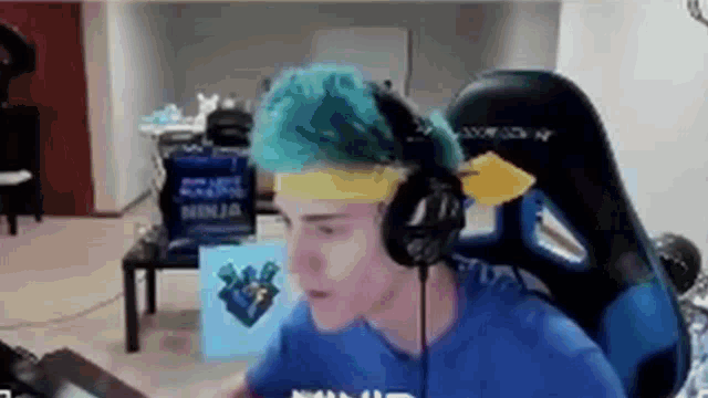 a man with blue hair and headphones is sitting in a chair .