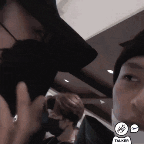 a man wearing a mask talks on a cell phone next to another man wearing a hat
