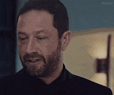 a man with a beard is wearing a black suit and a black shirt