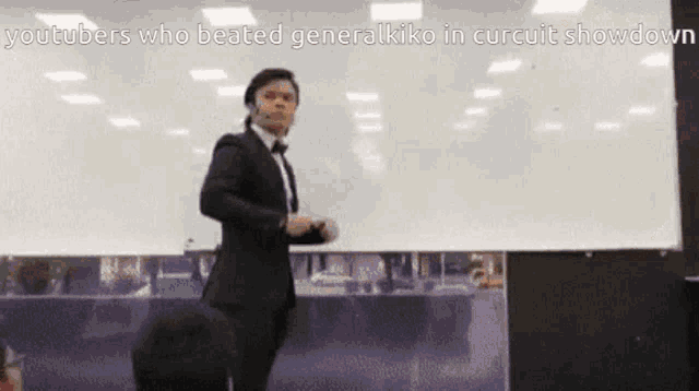 a man in a suit and bow tie is standing in front of a white board with the words youtubers who beat generalkiko in circuit showdown