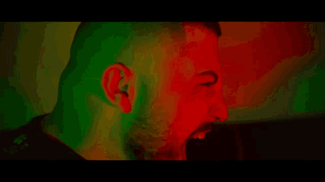 a close up of a man 's face in a dark room with red and green lights behind him .