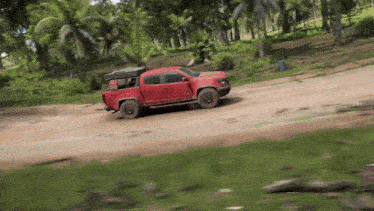 a red truck is driving down a dirt road in the woods