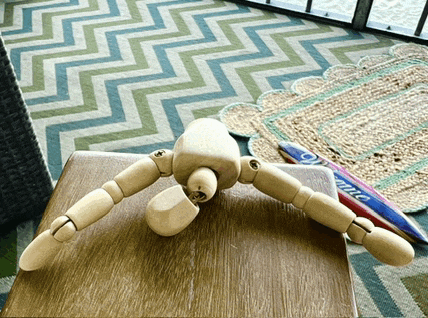a wooden mannequin is laying on a wooden table with a rug in the background