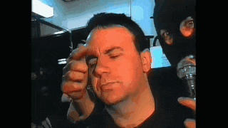 a man in a black shirt is getting his eyebrows done by another man in a mask