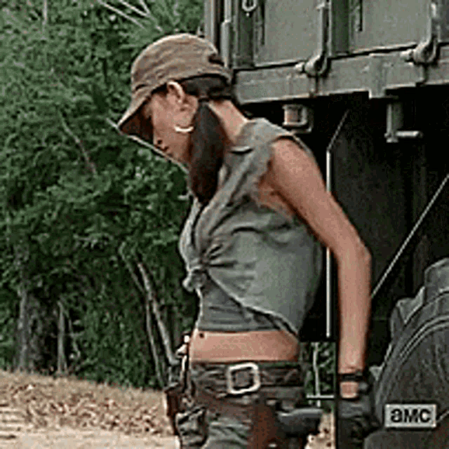 a woman wearing a hat and a crop top is standing in front of a truck that says amc on it