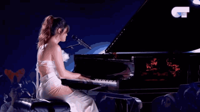 a woman in a white dress plays a grand piano