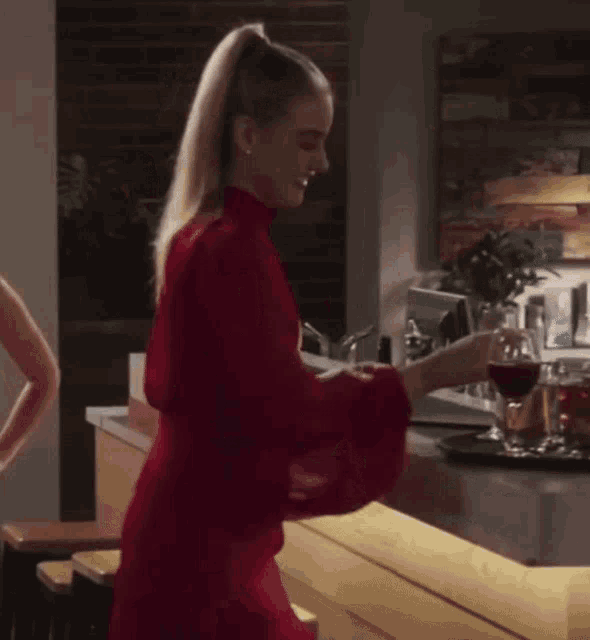 a woman in a red dress is standing in front of a bar holding a glass of wine