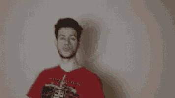 a man in a red shirt is standing in front of a wall holding a fan .