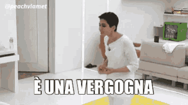 a woman in a white shirt is standing in a living room with the words e una verogna on the bottom
