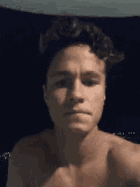 a young man without a shirt is taking a selfie in front of a dark background .