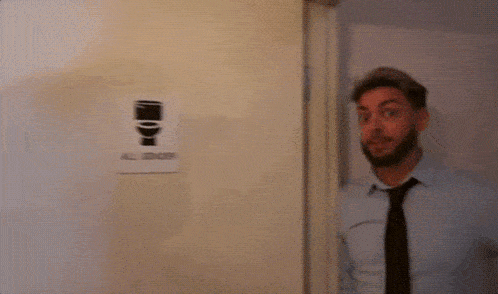 a man in a blue shirt and tie is standing in front of a sign that says ' men 's room ' on it
