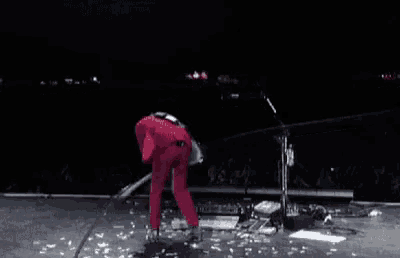 a man in a red jumpsuit is standing on a stage with a guitar in his hand .