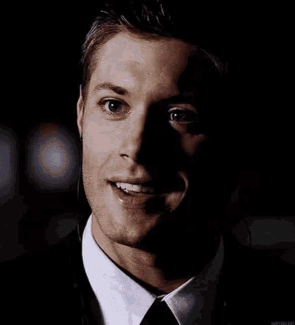 a man wearing a suit and tie is smiling in the dark .