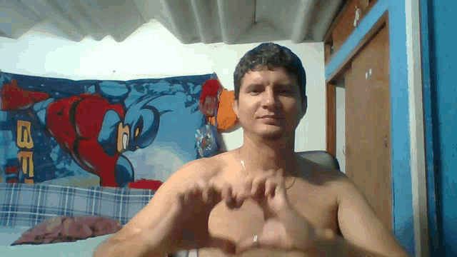 a shirtless man is making a heart with his hands in front of a spiderman tapestry