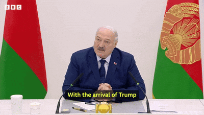 a man in a suit and tie is sitting at a desk with a sign that says with the arrival of trump