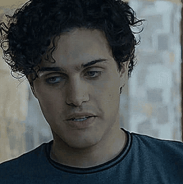 a close up of a man 's face with curly hair wearing a gray shirt .