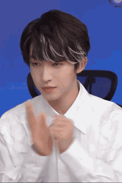 a young man wearing a white shirt with ruffles on the sleeves is clapping his hands