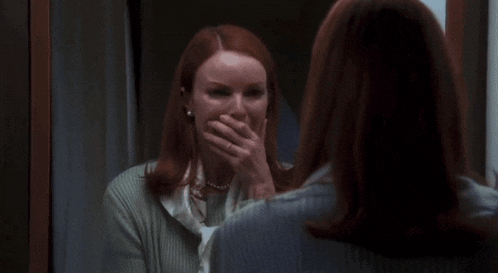 a woman with red hair is covering her mouth while looking at herself in the mirror