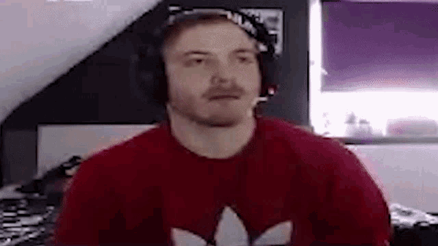 a man wearing headphones and a red shirt is sitting in front of a computer screen .