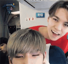 two young men are sitting on a plane with a blue exit sign behind them