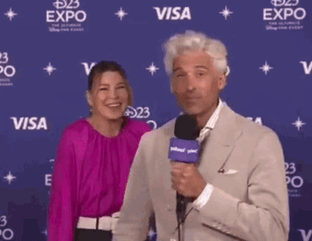 a man and a woman are standing next to each other on a red carpet . the man is holding a microphone .