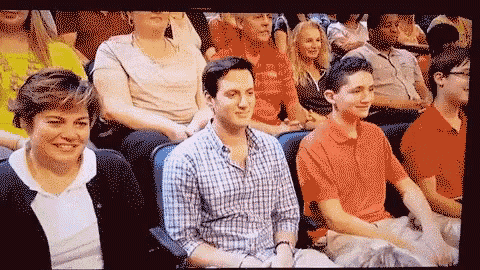 a group of people are sitting in a stadium and one of them is wearing a plaid shirt