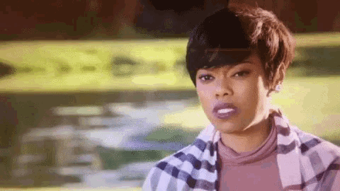 a woman with short hair is wearing a plaid shirt and a pink turtleneck .